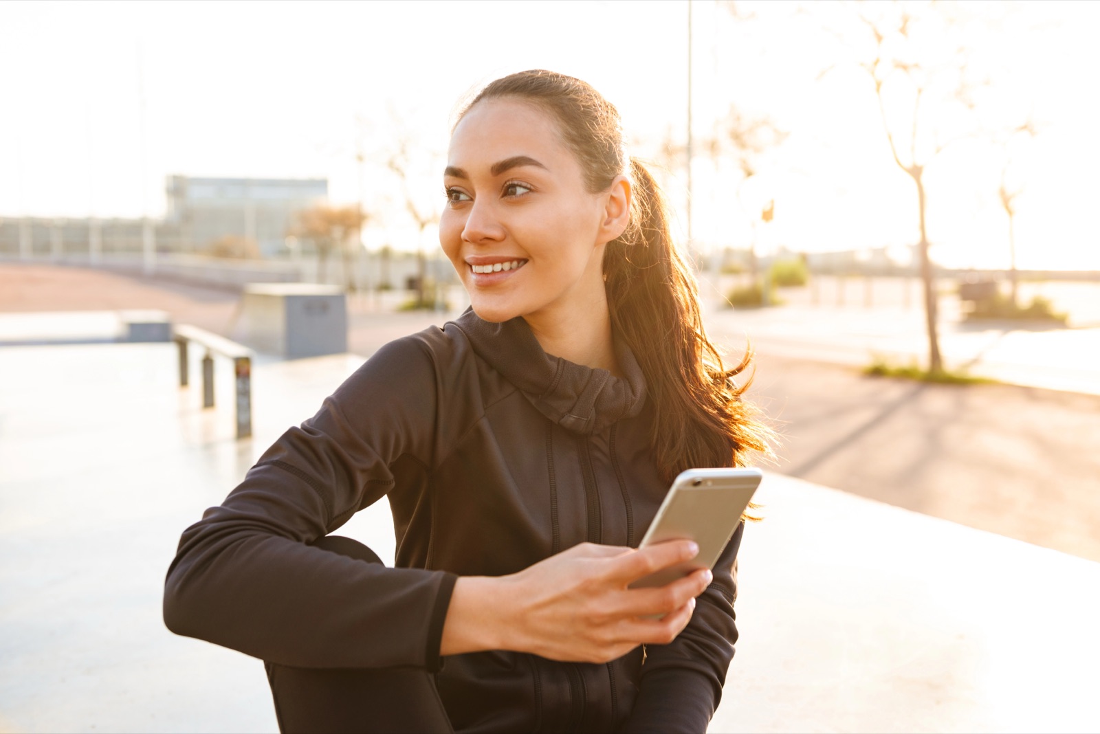 Young woman sitting outdoors using mobile phone for fitness